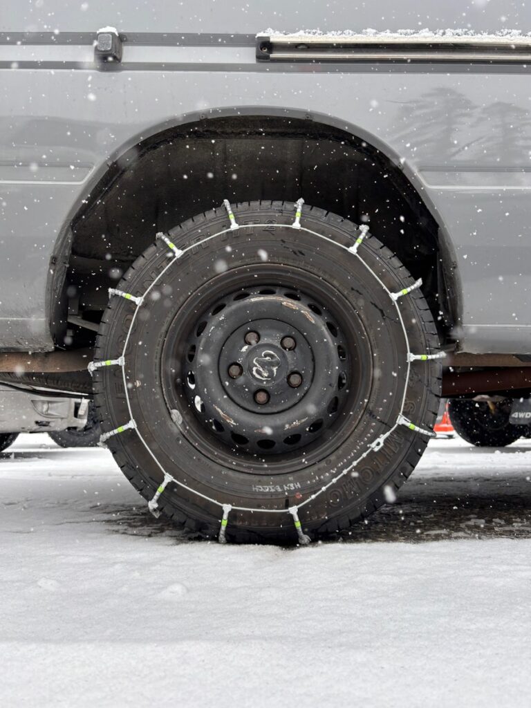 Snow chains are on a car tire in snow.