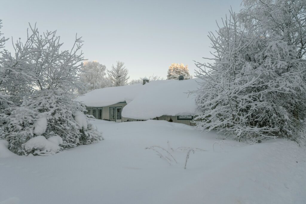 a house covered in snow next to trees