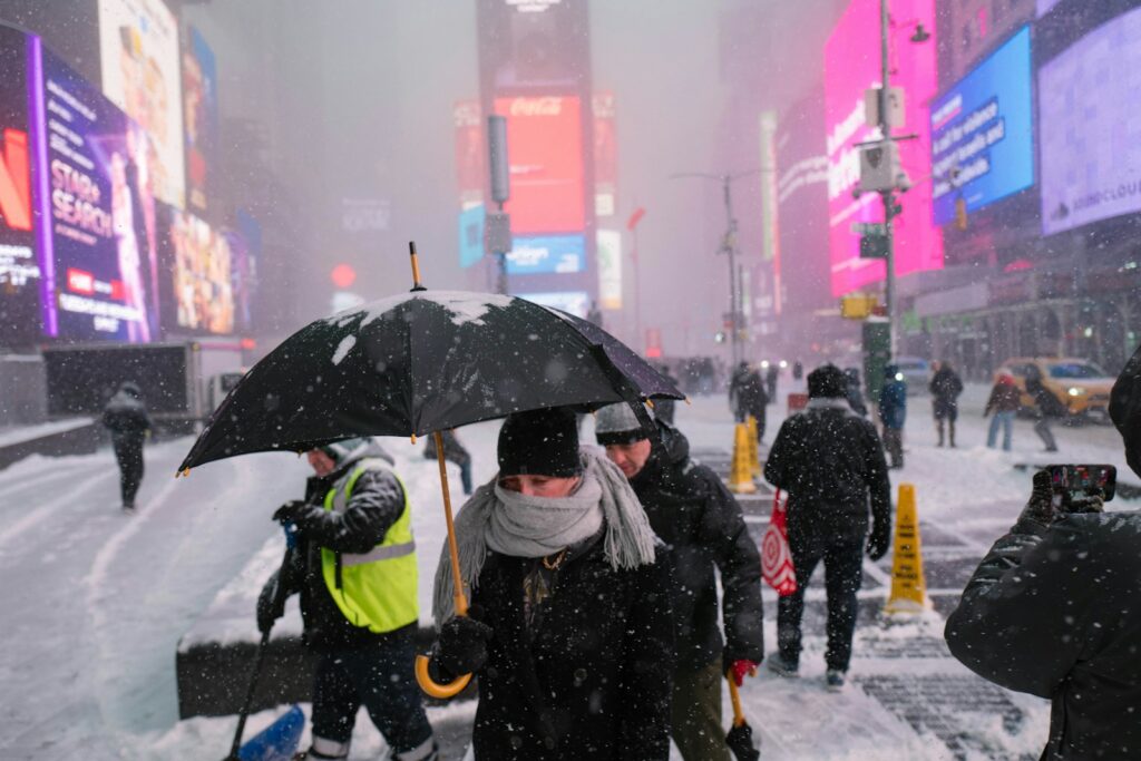 People with umbrellas walk through snowy times square.